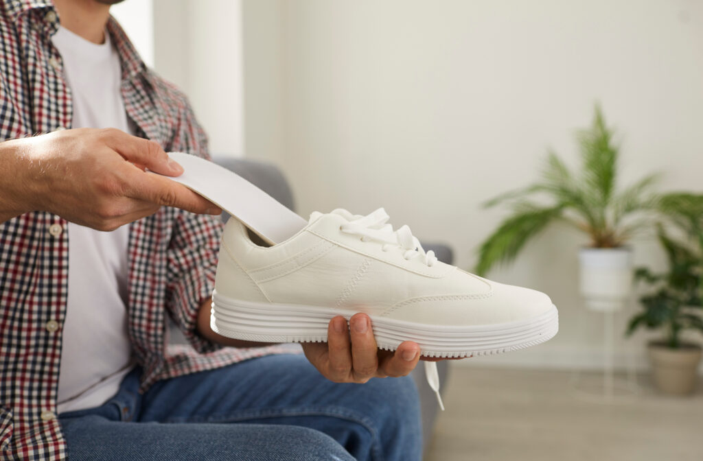 Mladý muž vkládá novou čistou stélku do moderní bílé pohodlné sportovní boty, kterou drží v ruce.