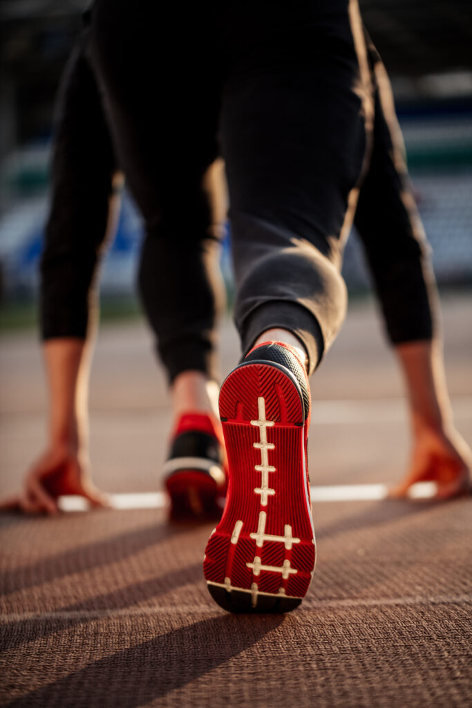 Zadní pohled na nohu běžce na začátku dráhy na stadionu. Červená podrážka běžeckých bot.