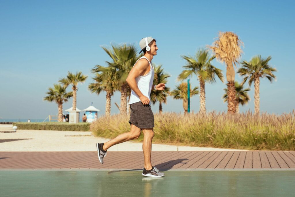 Mladý muž běží v pánské sportovní obuvi, v pozadí jsou palmy a pláž