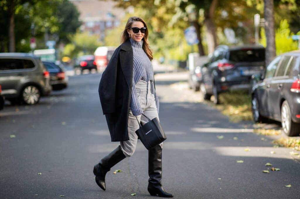 žena ve svetru, černém kabátu, džínách a černých kovbojských botách