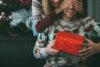 Tip na vánoční dárek pro něj - žena dává dárek muži, oba mají na sobě vánoční svetry