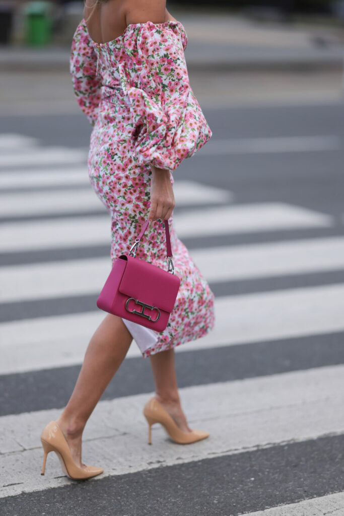 Žena v květinových šatech s pufovanými rukávy se sytě růžovou kabelkou a béžovými lakovanými lodičkami