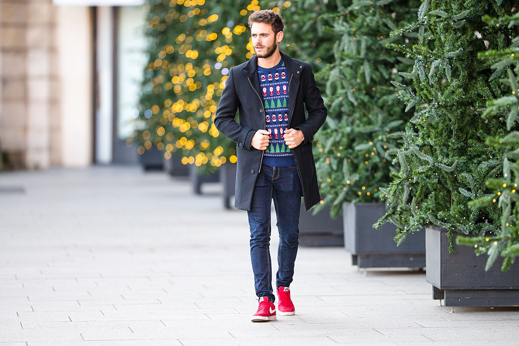 Muž oblečený v kabát a vánoční svetr a na nohou má červené tenisky